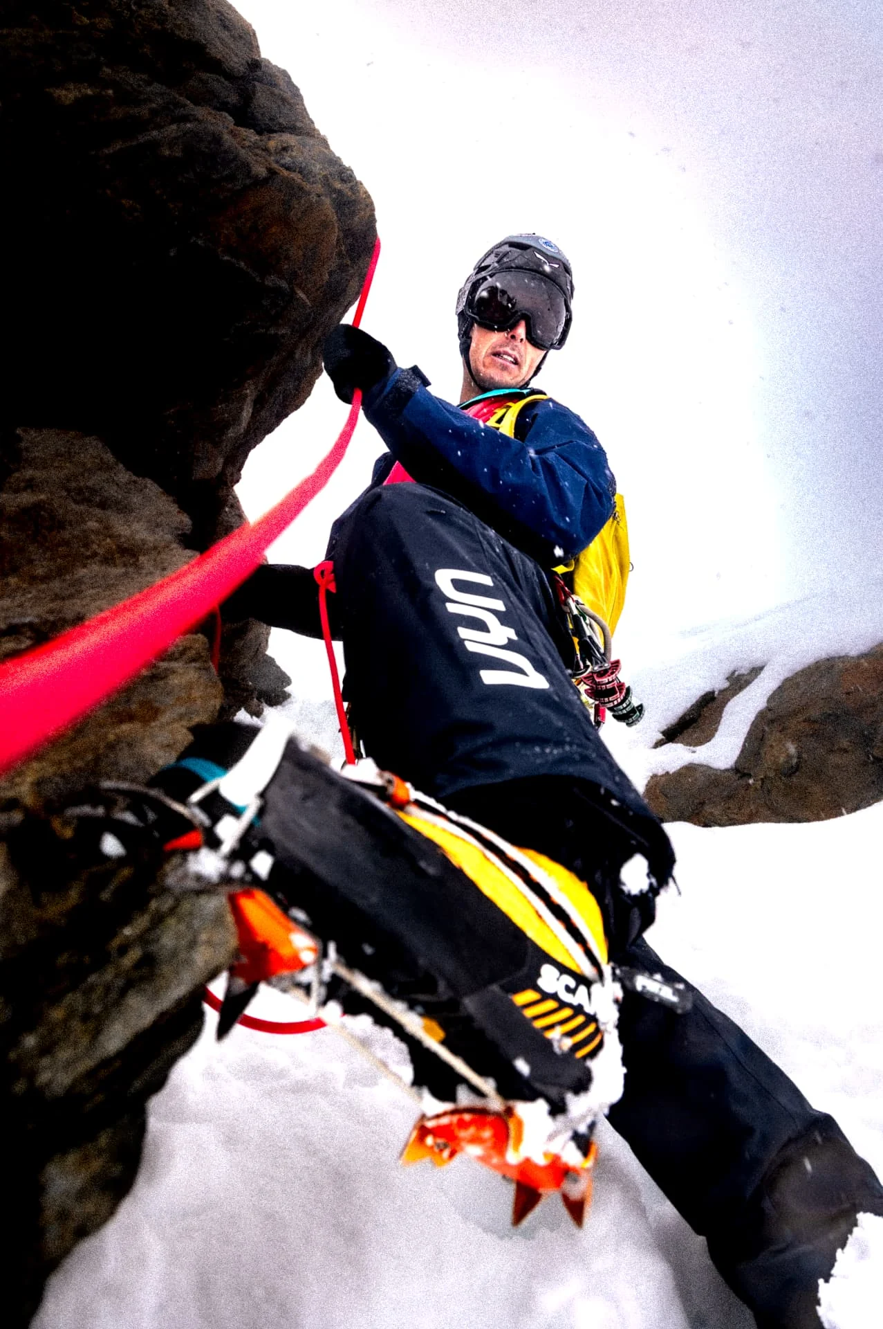 Alpinist with crampons and a red rope on snow and rock, shot from above