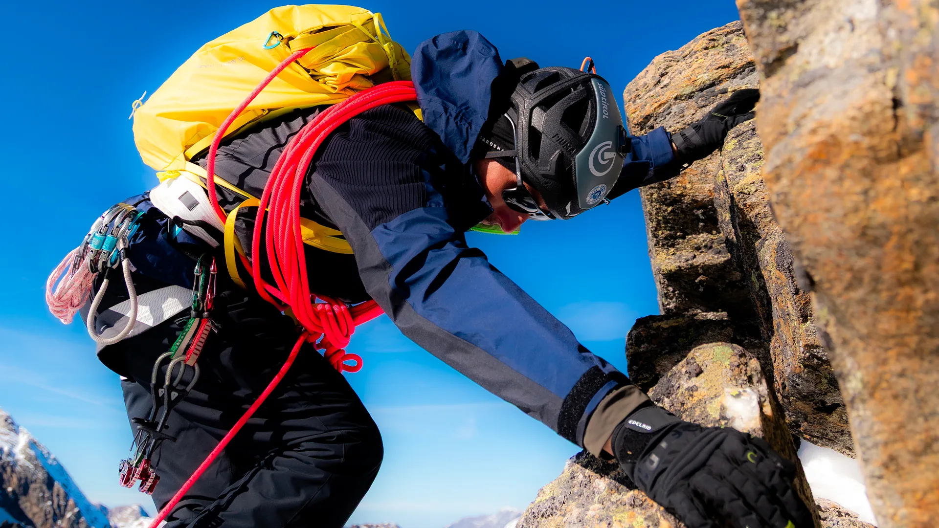 Alpinist with a coiled red rope climbing a steep rocky ridge