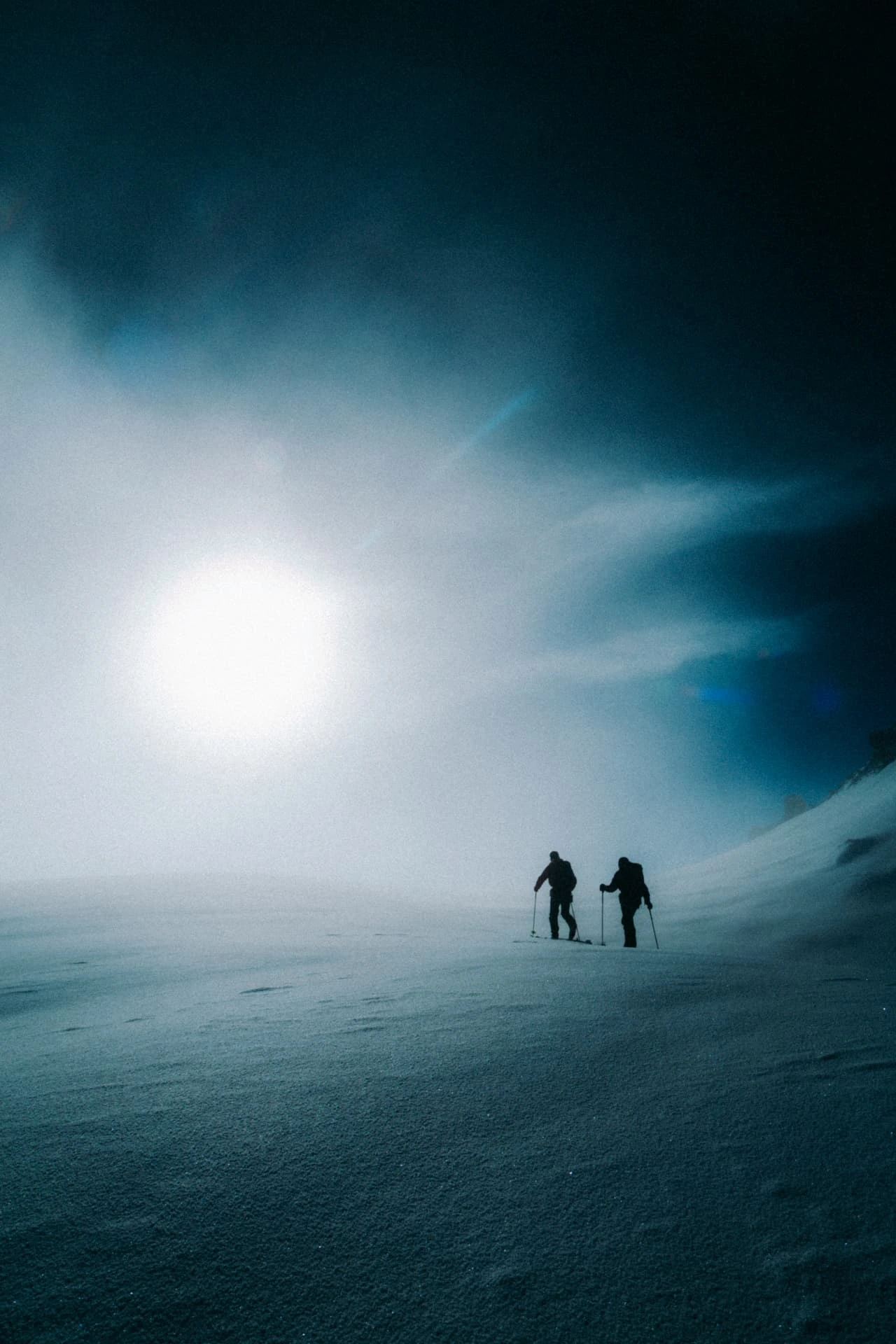 Two ski tourers in silhouette under a hazy sun