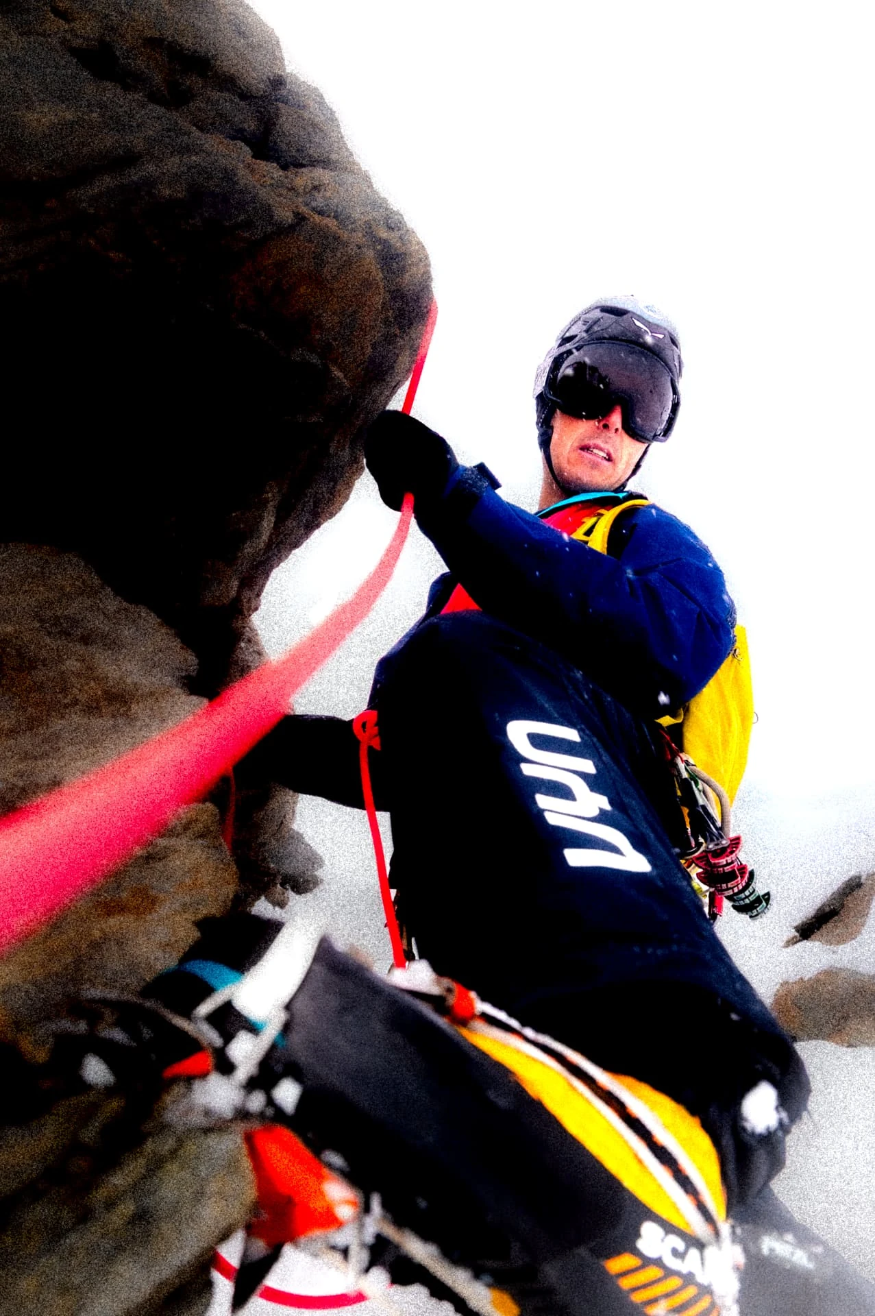 Alpinist with crampons and a red rope on snow and rock, shot from above