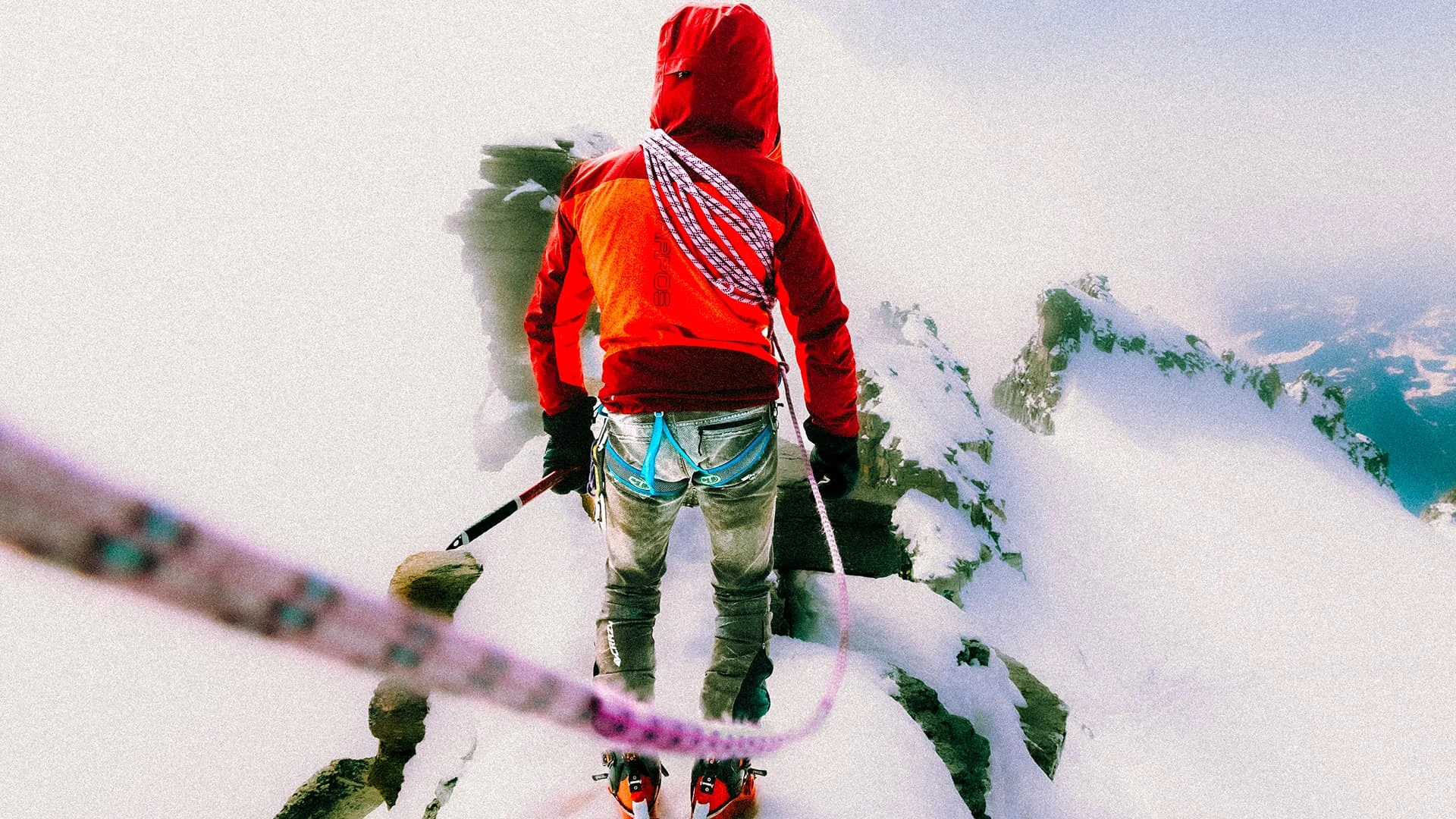 Alpinist in red standing on a snowy summit ridge