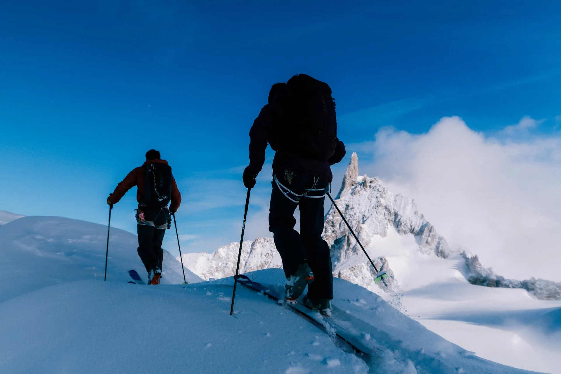 Two ski tourers climbing a snowy ridge towards a granite spire