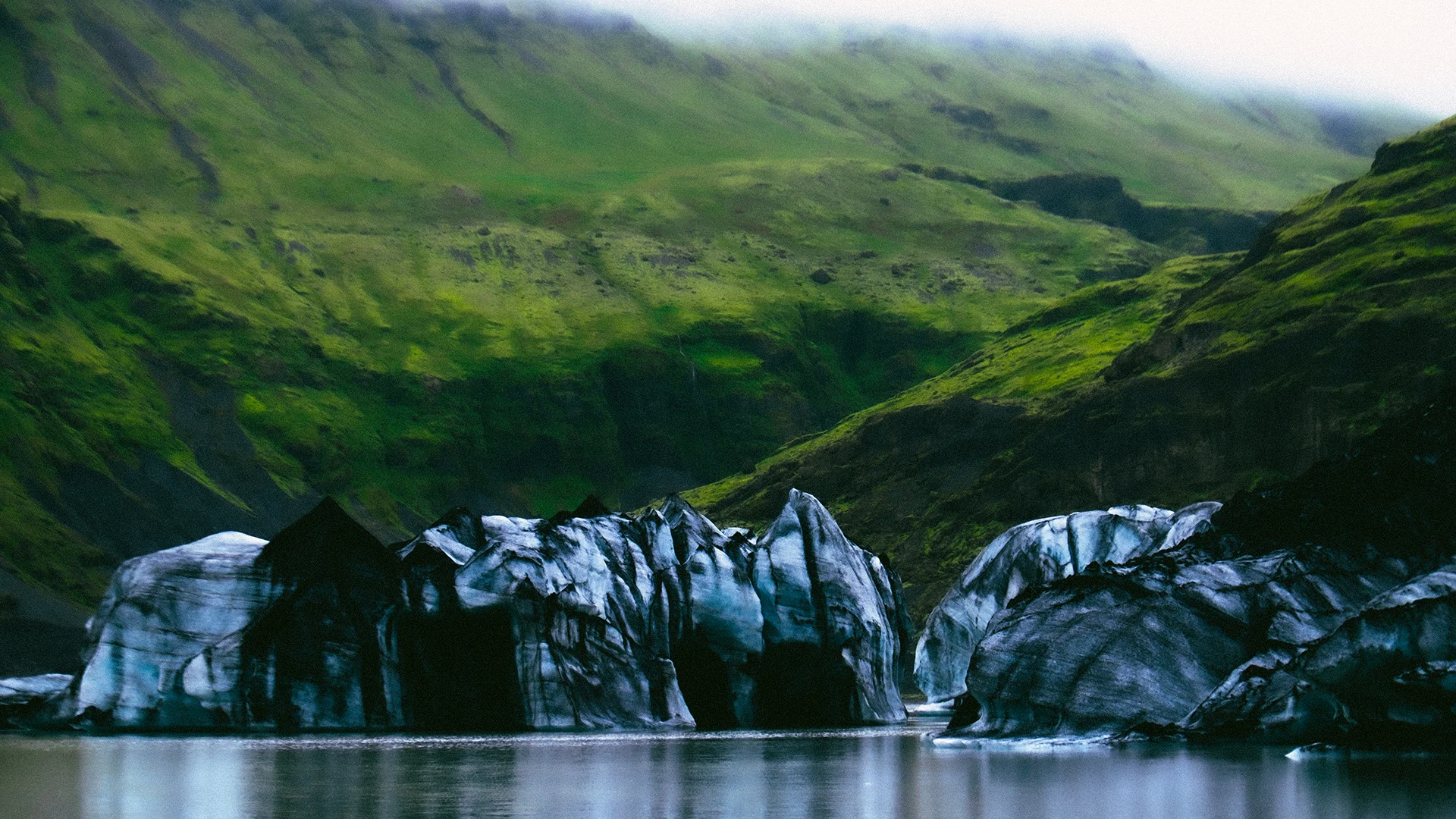Blue glacier reflected in a lagoon beneath green mountains