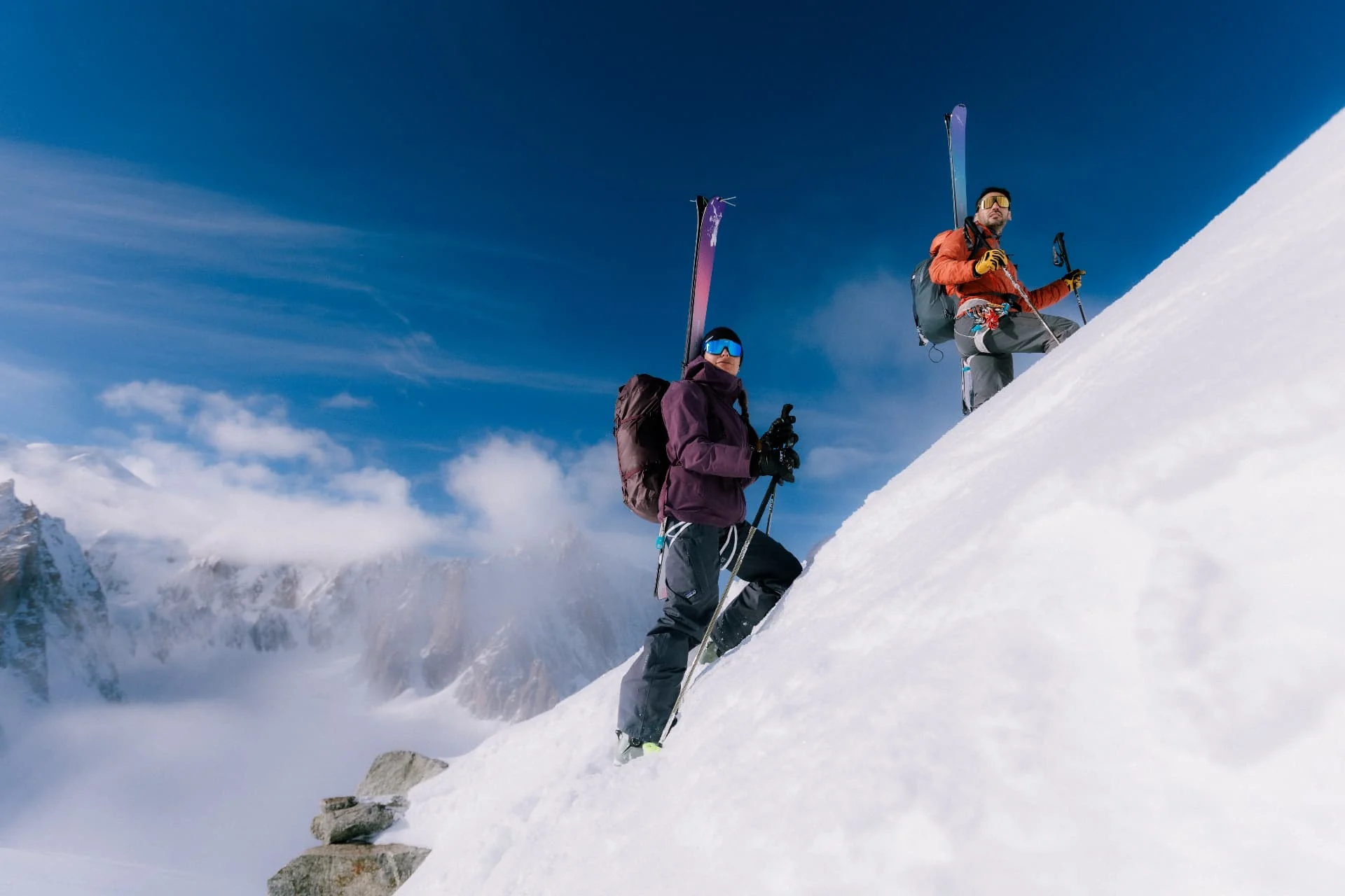 Two ski tourers climbing a steep snowy slope under a deep blue sky