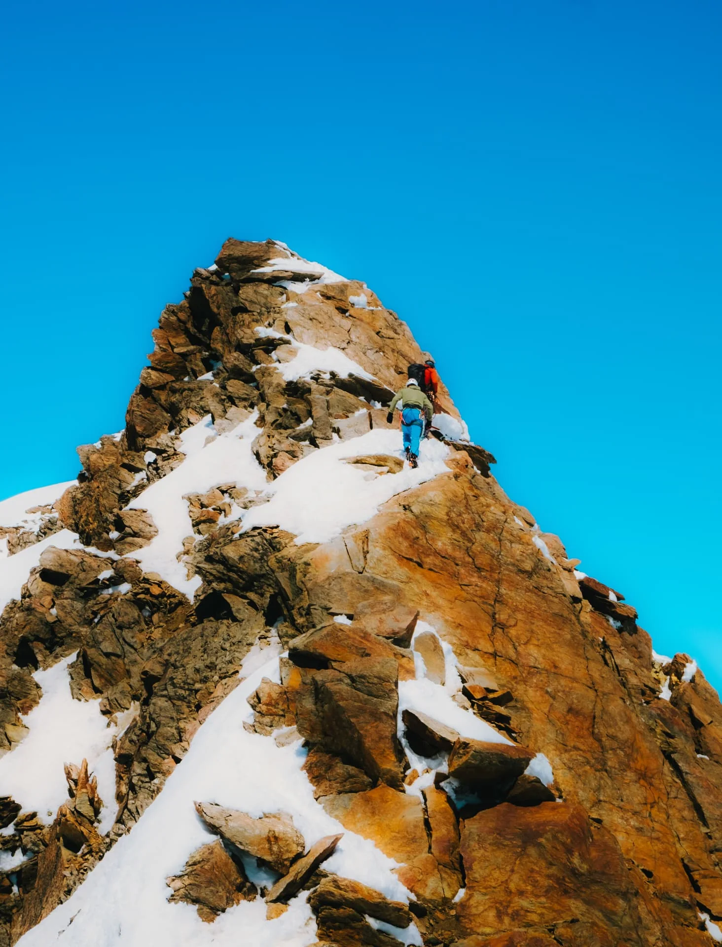 Mountaineers ascending a rocky snow-covered summit
