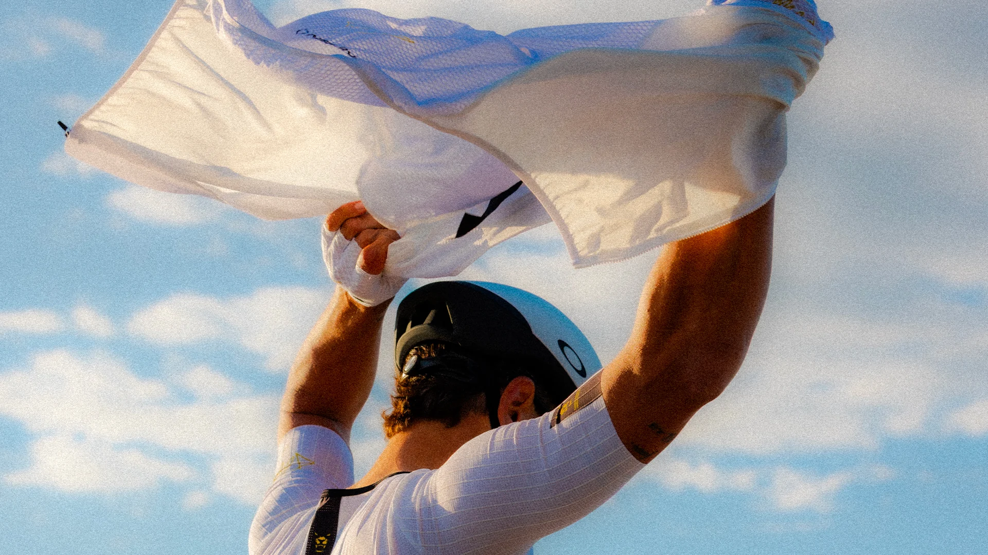 Cyclist lifting a white jersey beneath an open sky