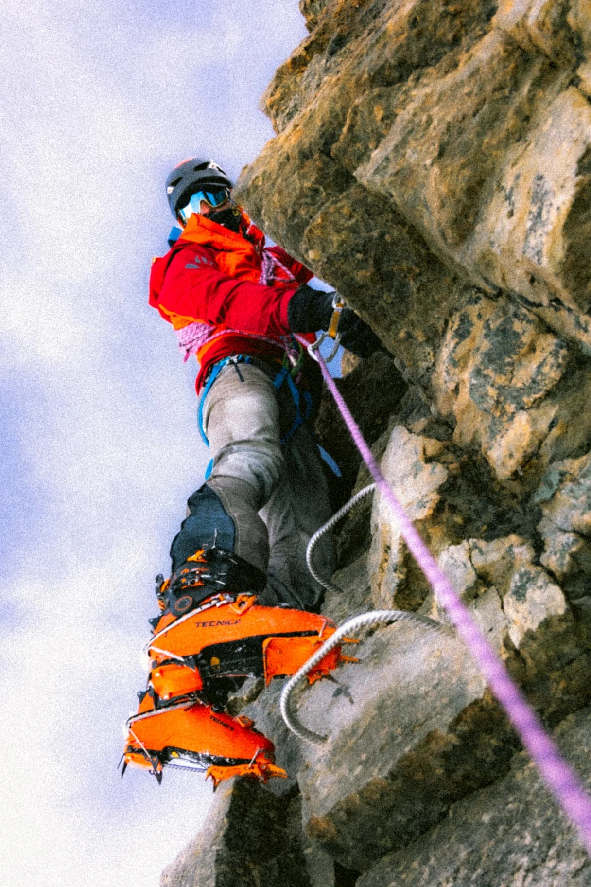 Climber in a red jacket with orange crampons on a rocky wall