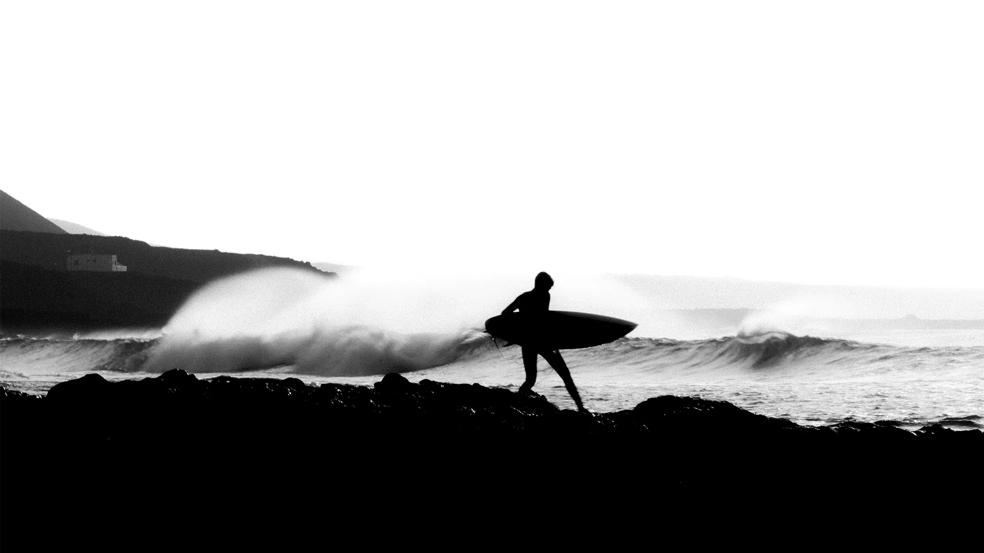 Black and white silhouette of a surfer walking over coastal rocks