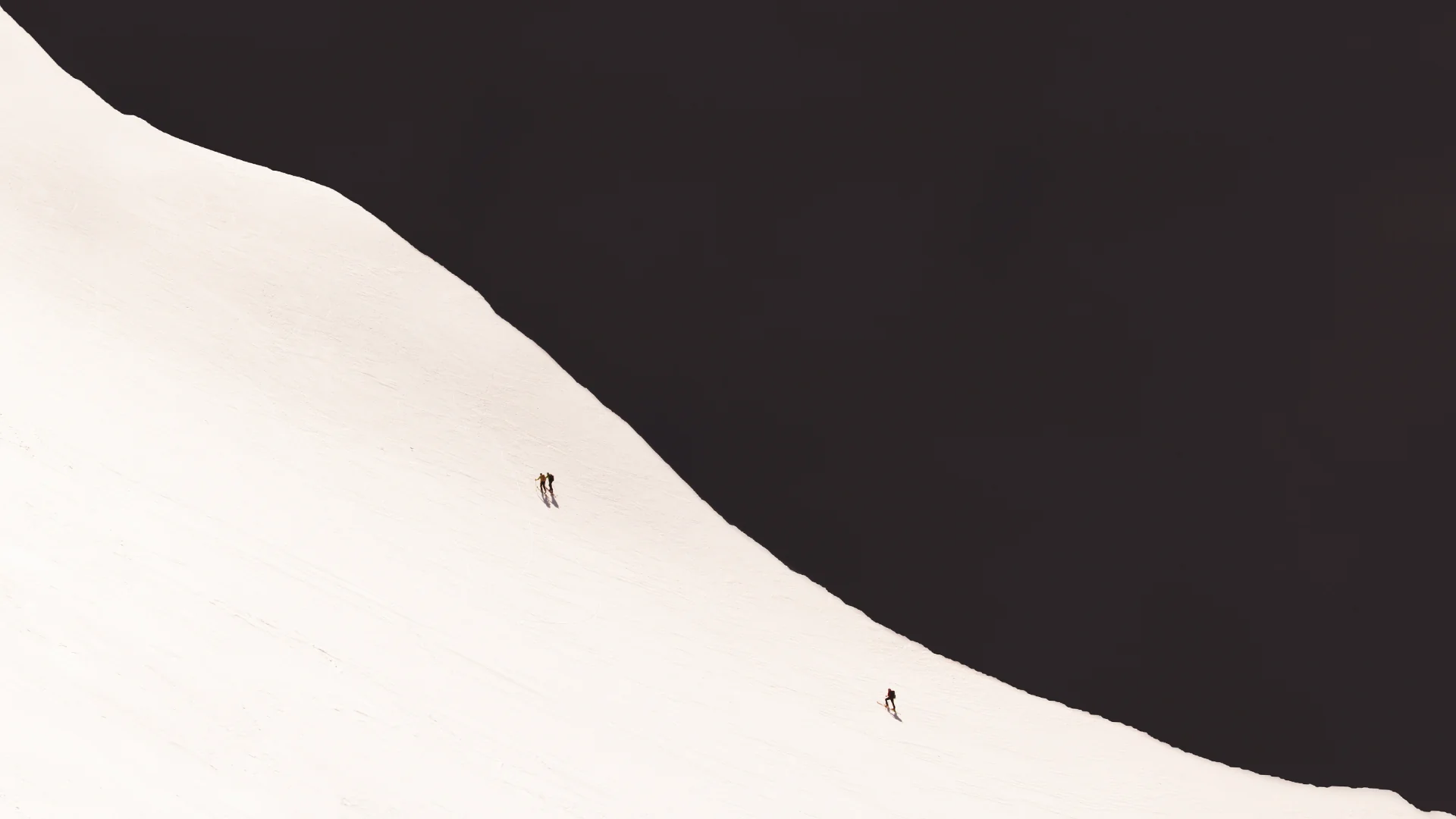 Three mountaineers crossing the curve of a vast snowy slope