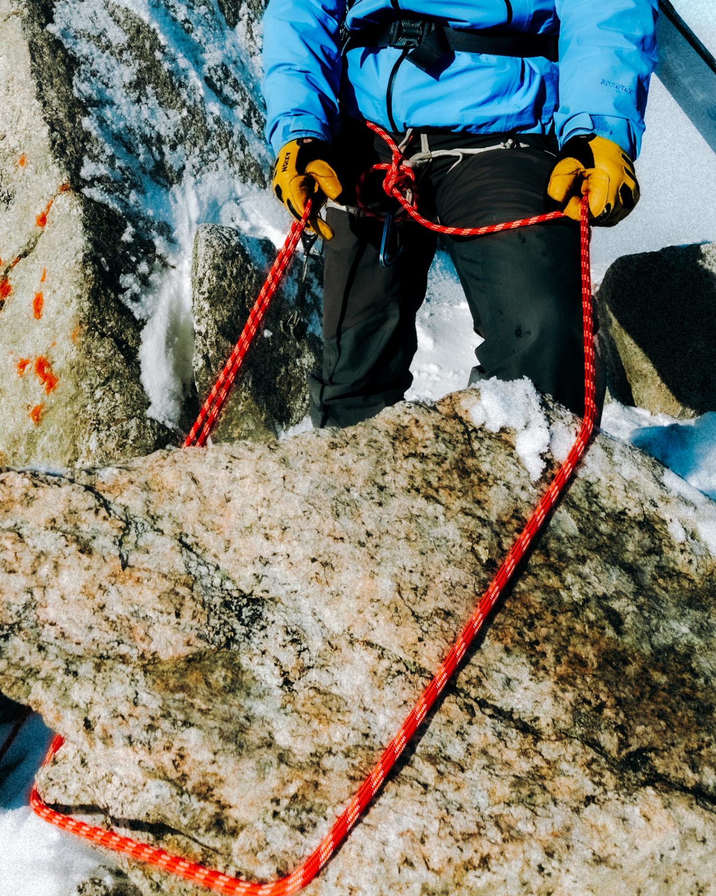 Alpinist with harness and red rope on snowy granite