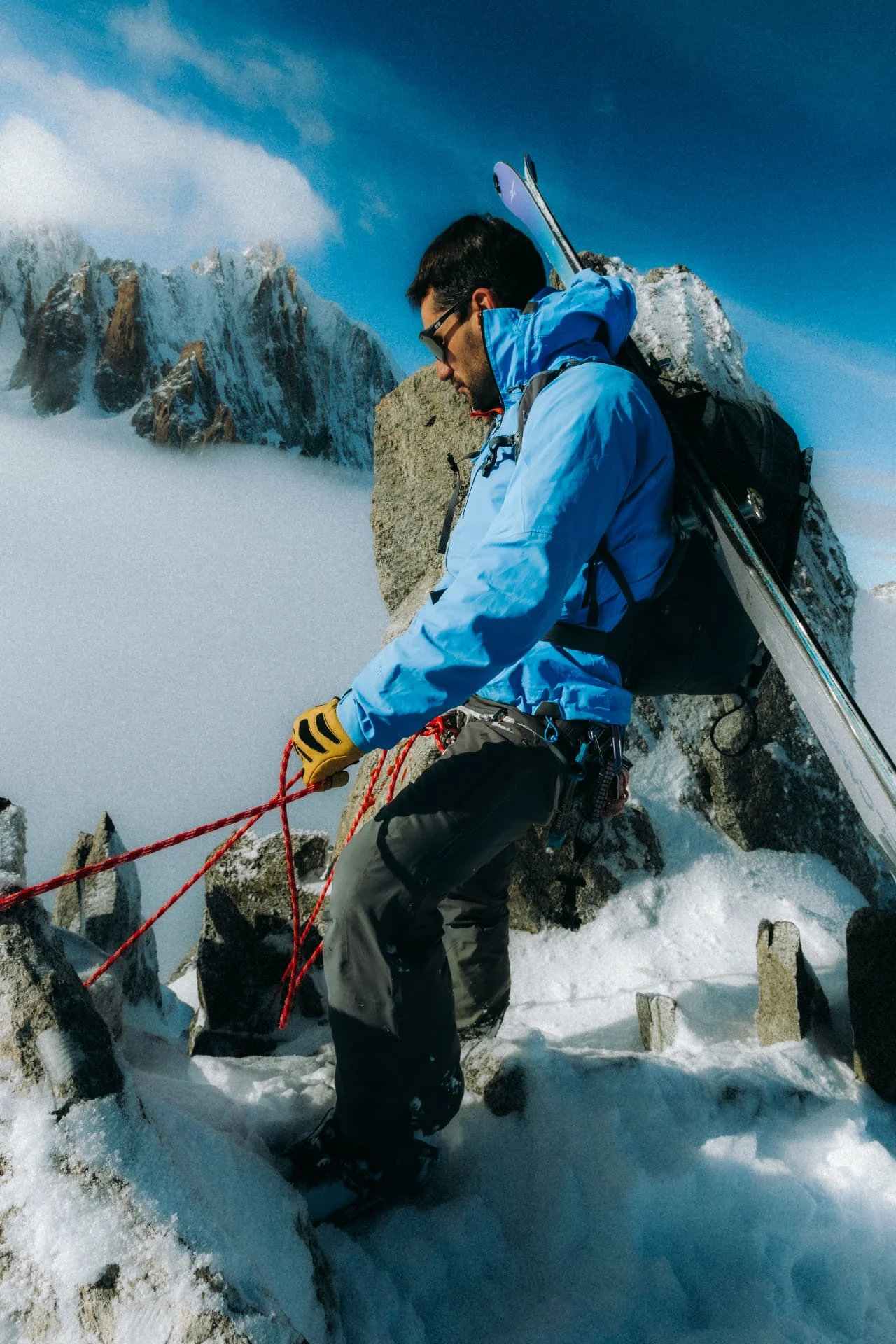 Skier in a blue jacket rappelling among snowy granite rocks