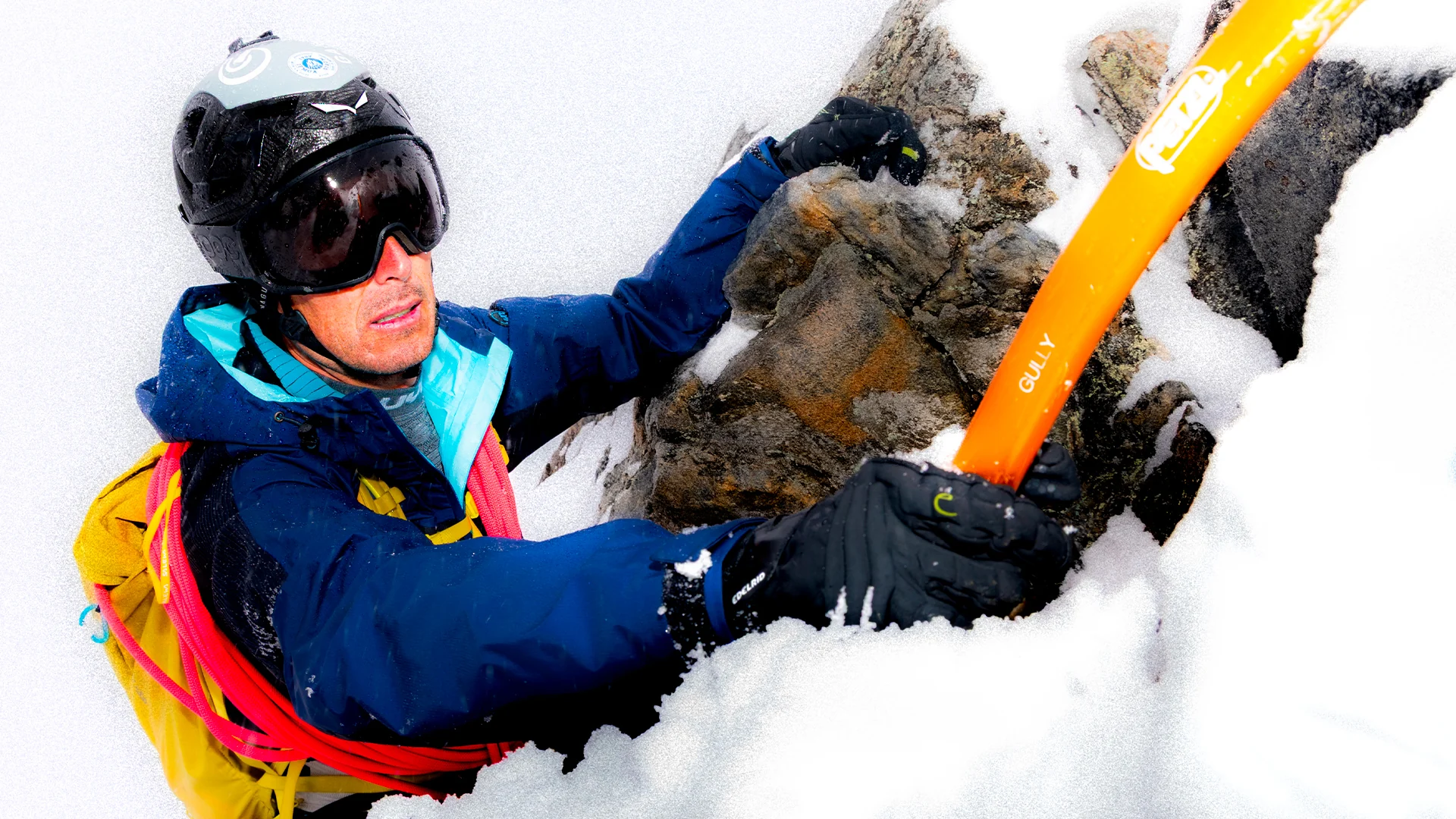 Alpinist climbing snow-covered rock with an orange ice axe