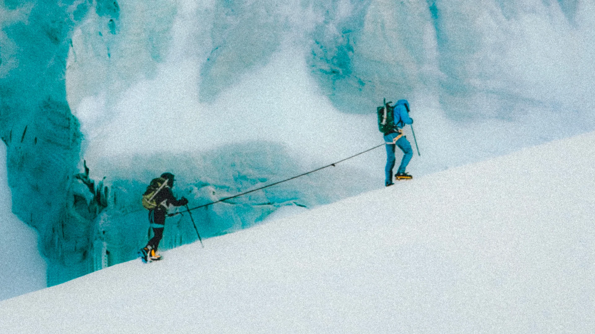 Roped alpinists climbing alongside a blue glacier wall