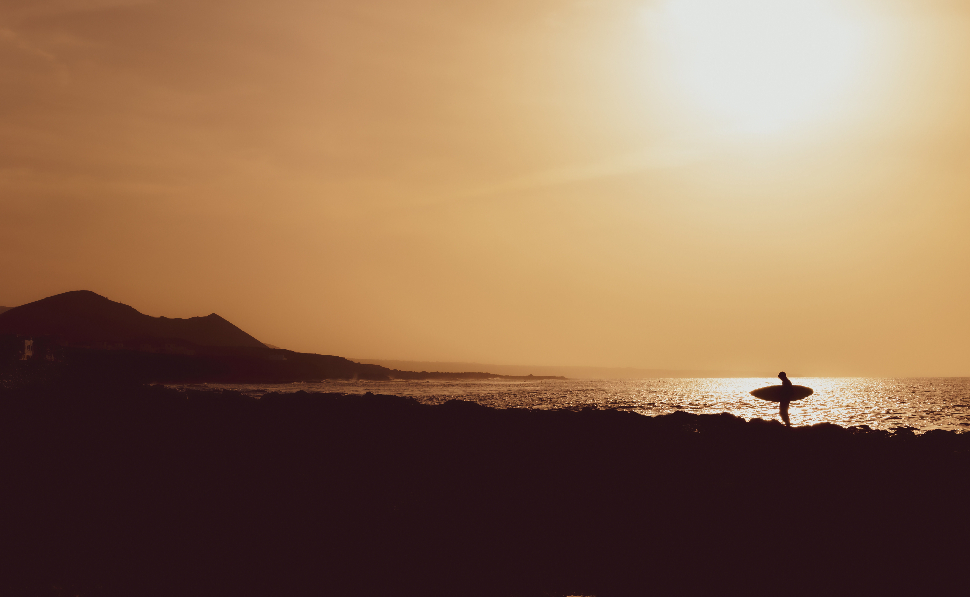 Silhouette of a surfer at sunset with a volcano in the background