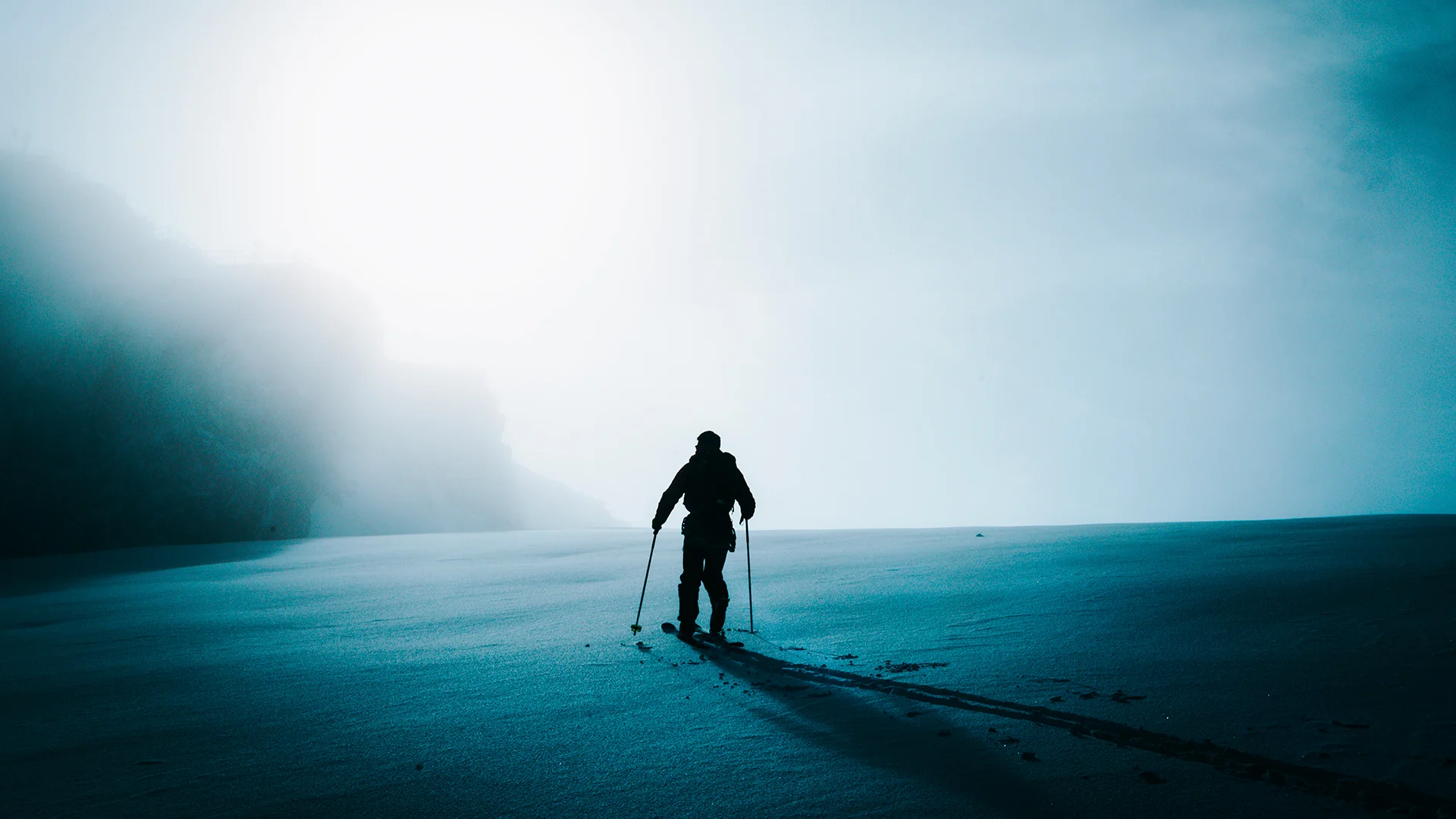 Lone ski mountaineer crossing a blue snowfield in misty light