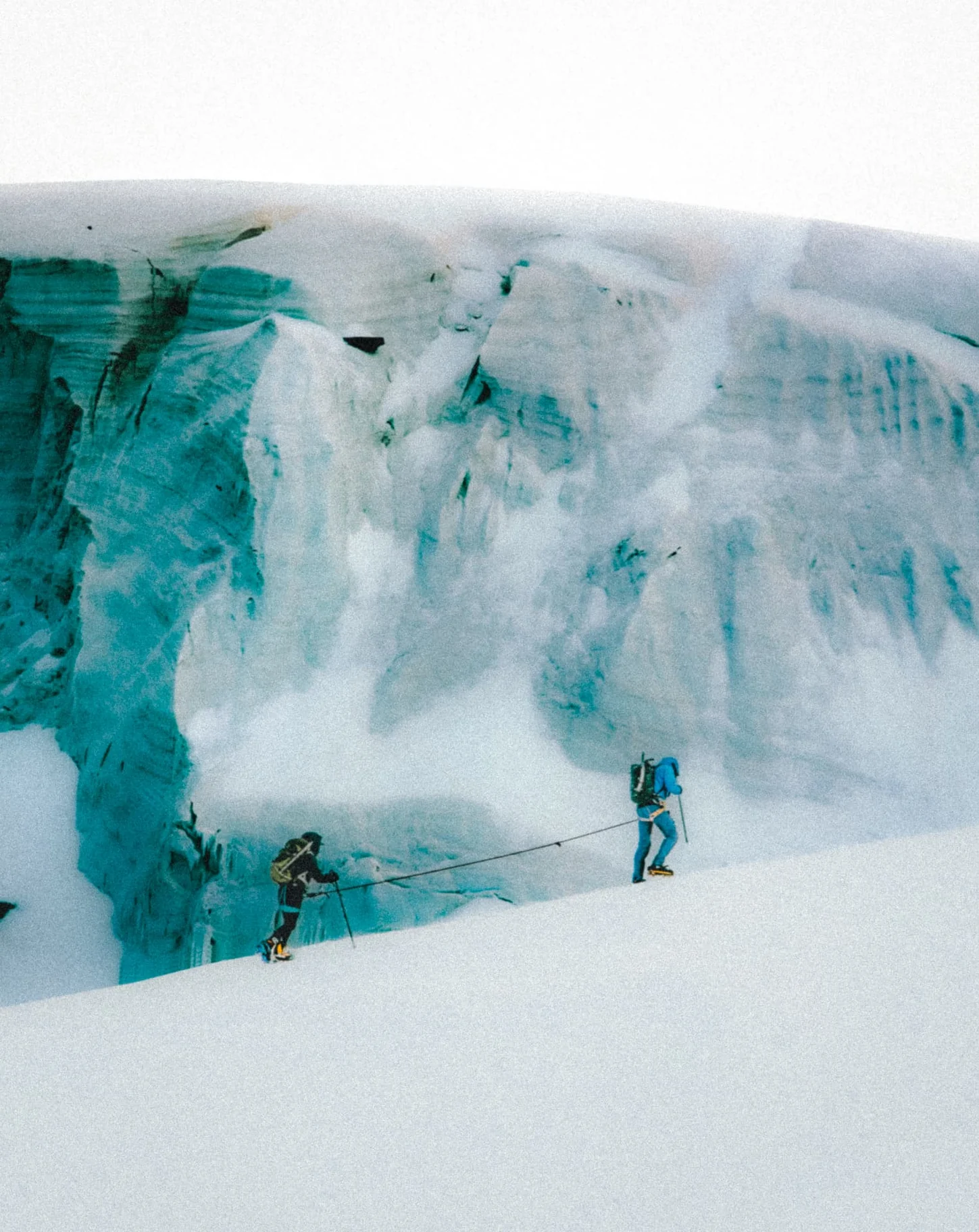 Two roped alpinists crossing a glacier beneath a turquoise icefall