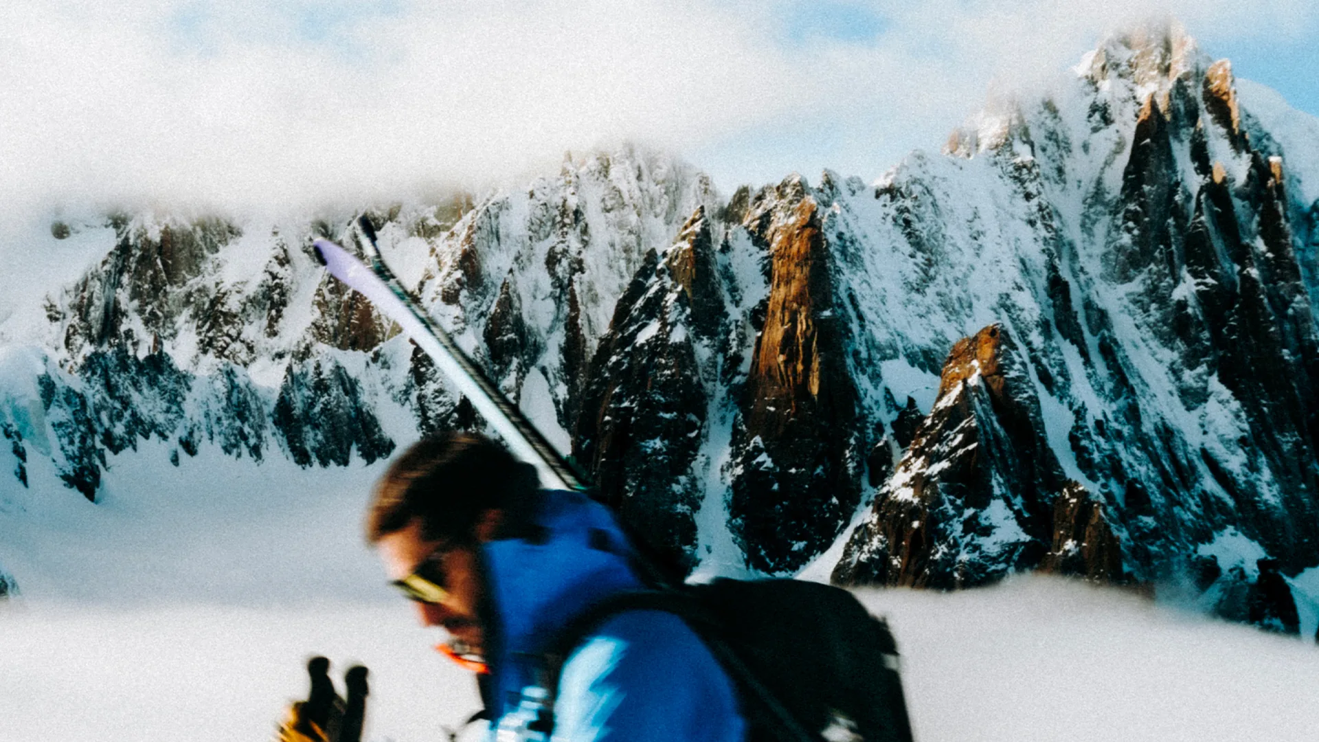 Skier with skis on his backpack passing in front of jagged granite peaks