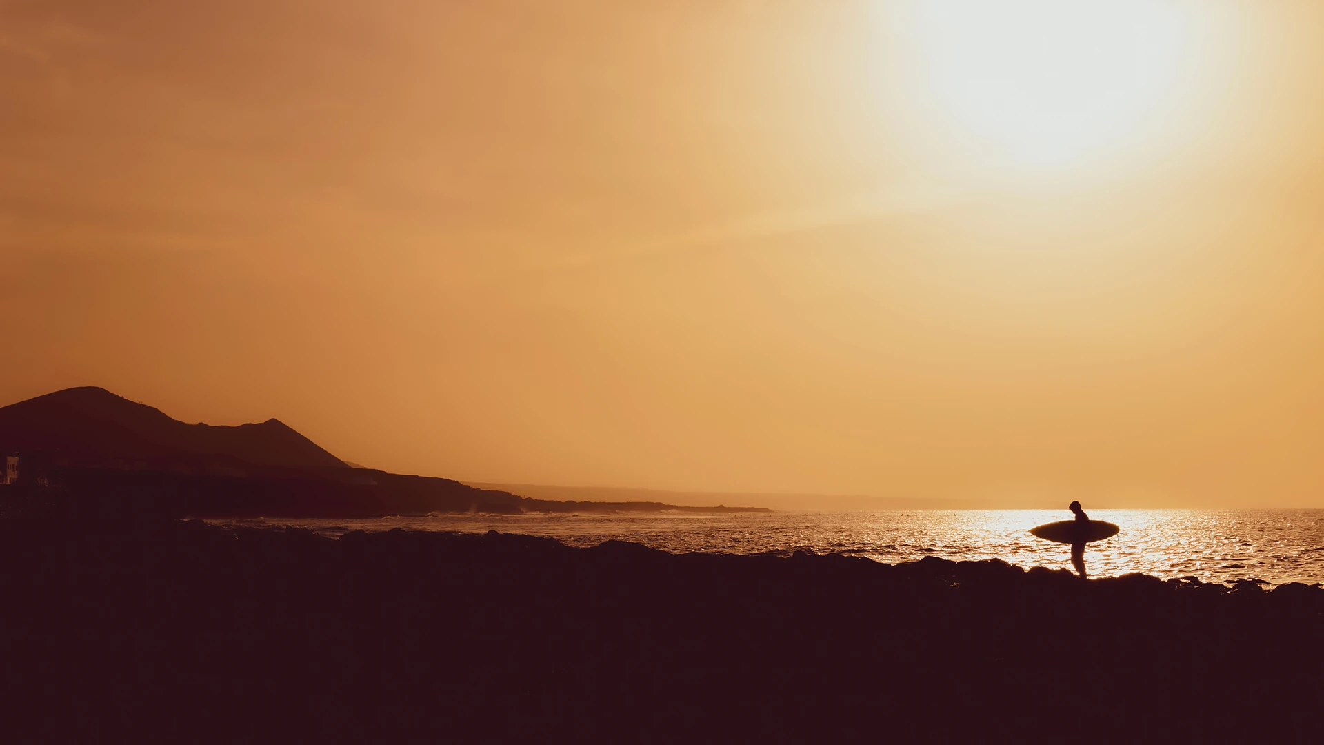 Silhouette of a surfer with a board on the rocks under a golden sky — fine art prints for your home