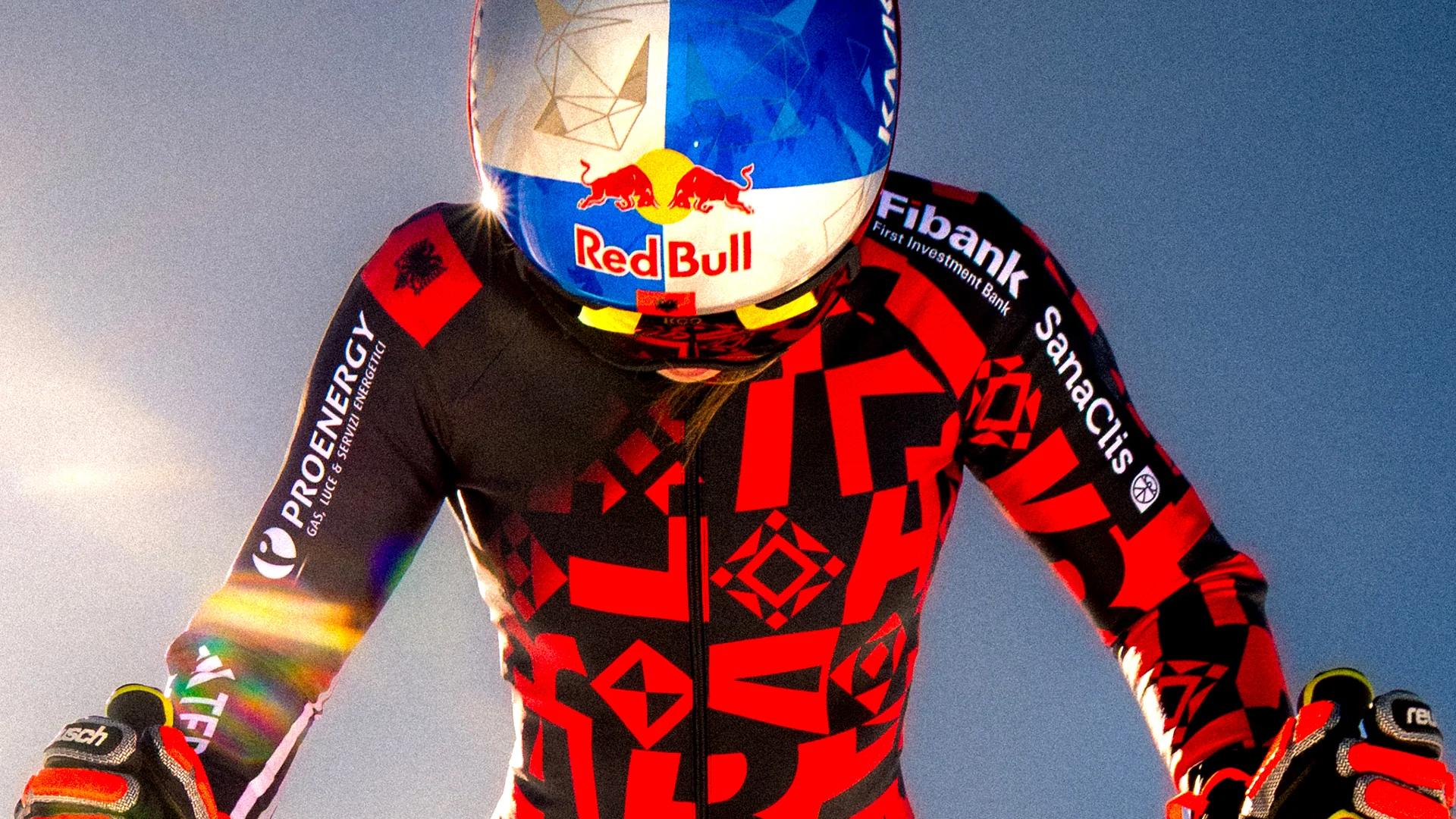 Ski racer in a red and black suit beneath dramatic light