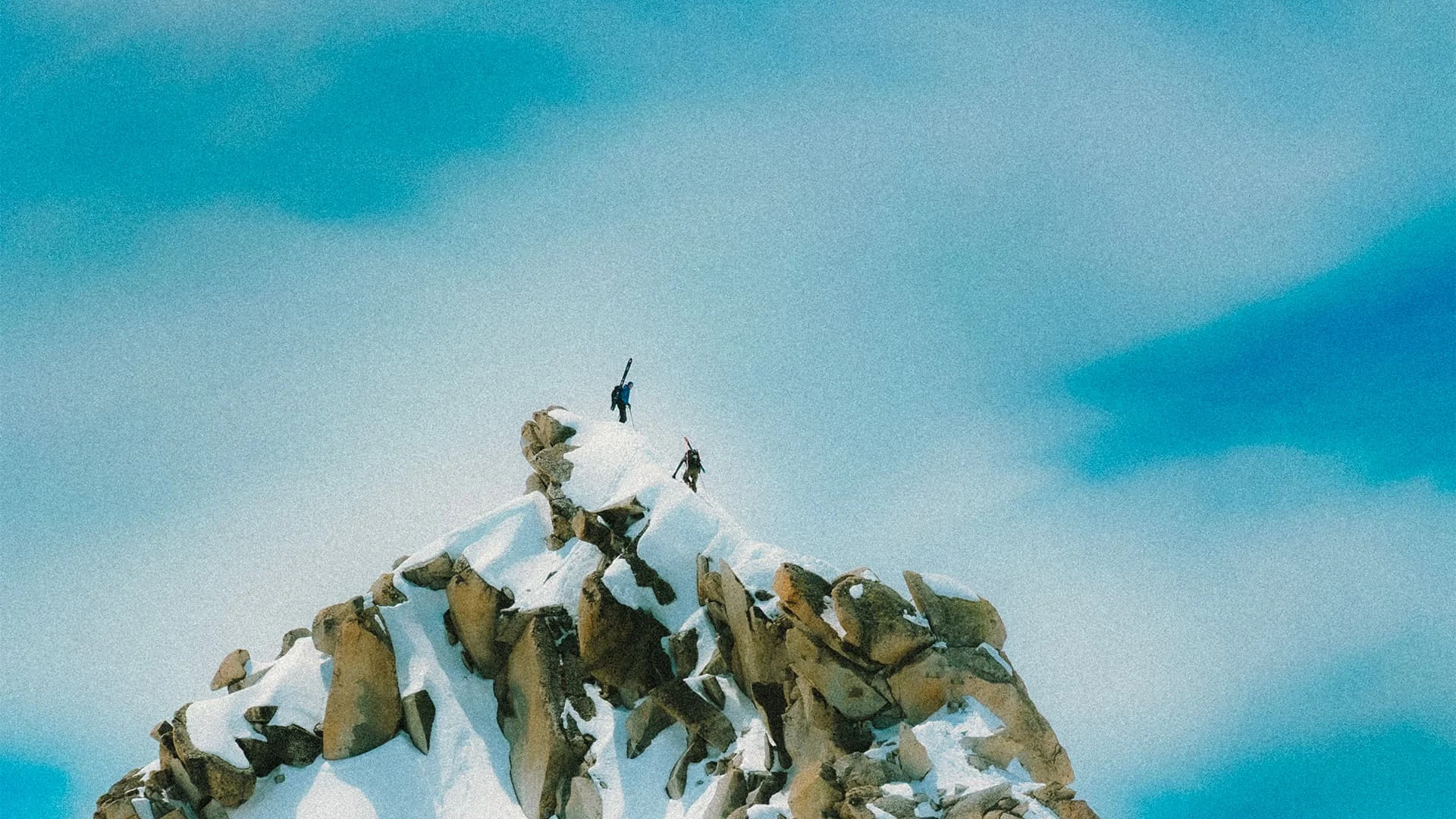 Two mountaineers reaching the top of a snowy rocky peak