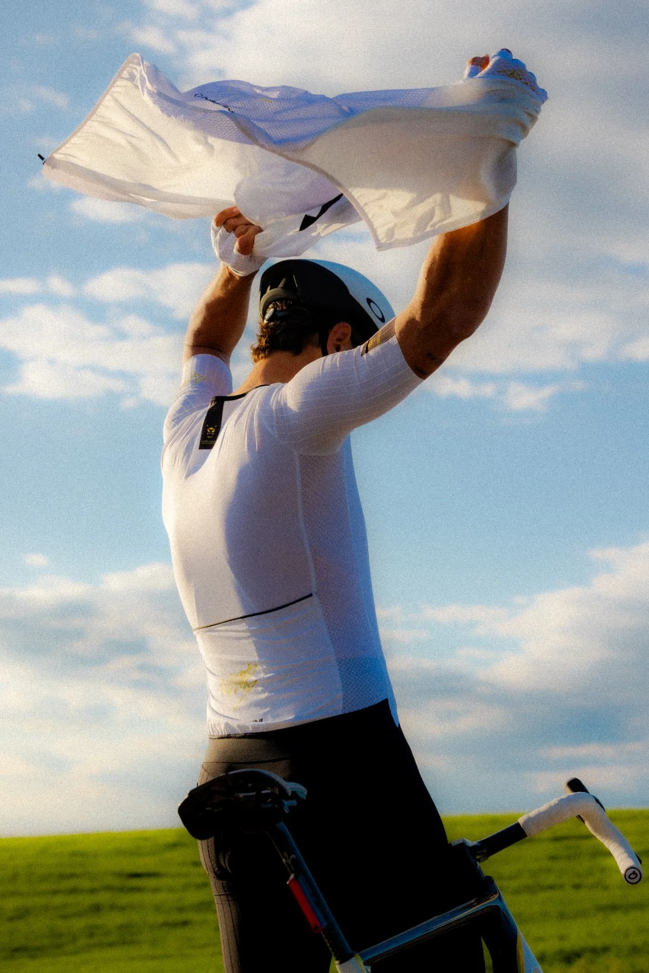 Cyclist lifting a white jersey beneath an open sky