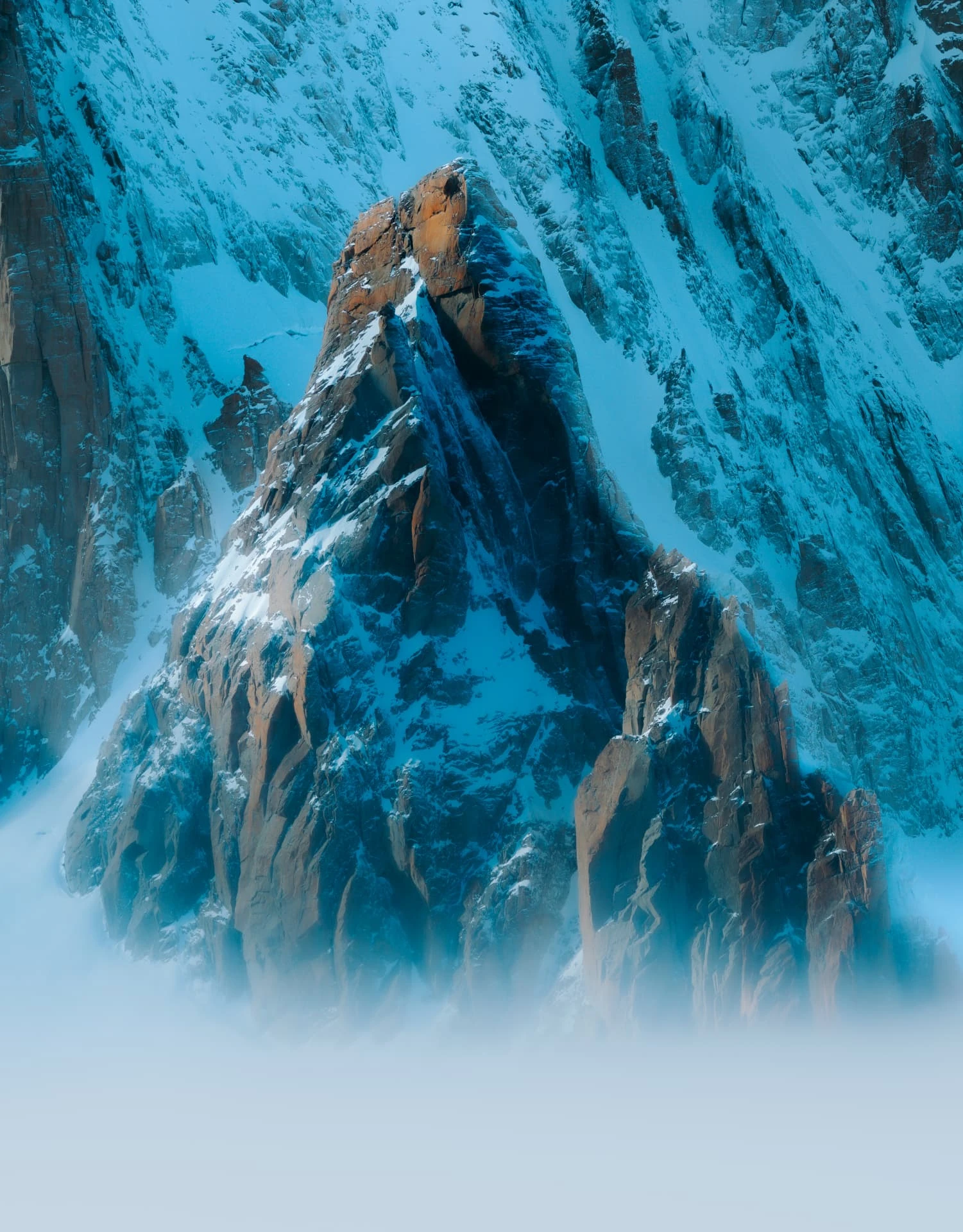 Snow-covered rock spire with a sunlit summit emerging above mist