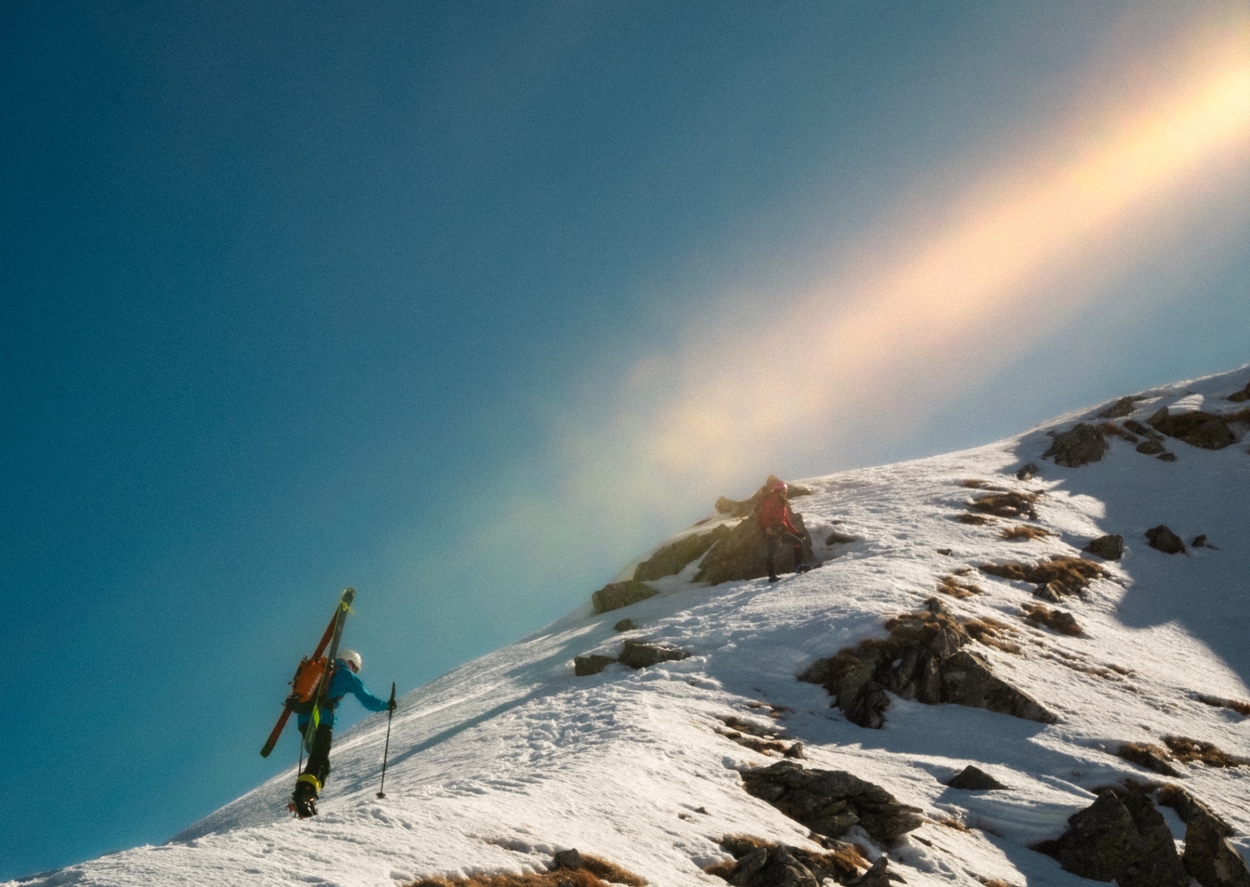Ski tourers climbing with a rainbow of clouds in the sky