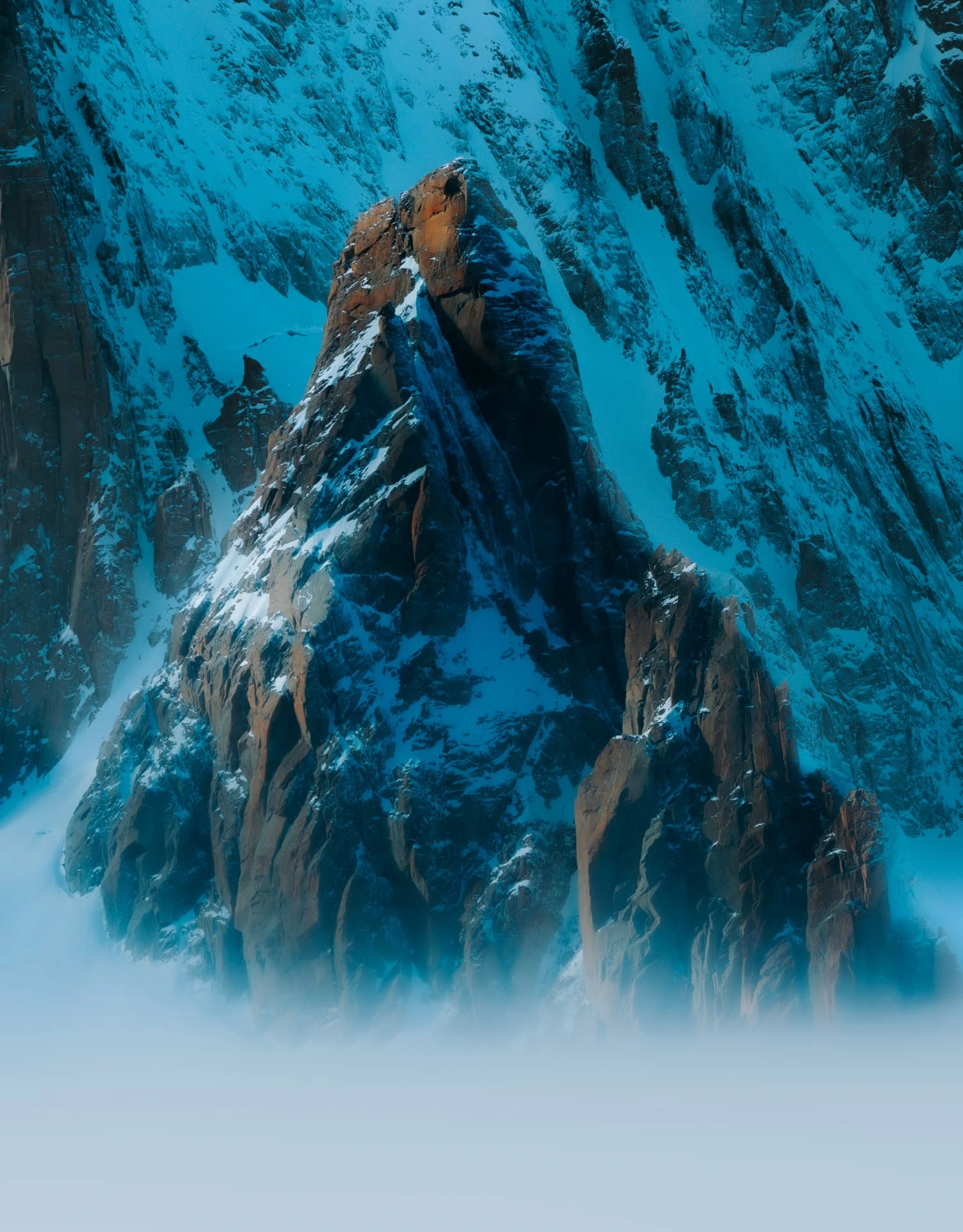 Snow-covered rock spire with a sunlit summit emerging above mist