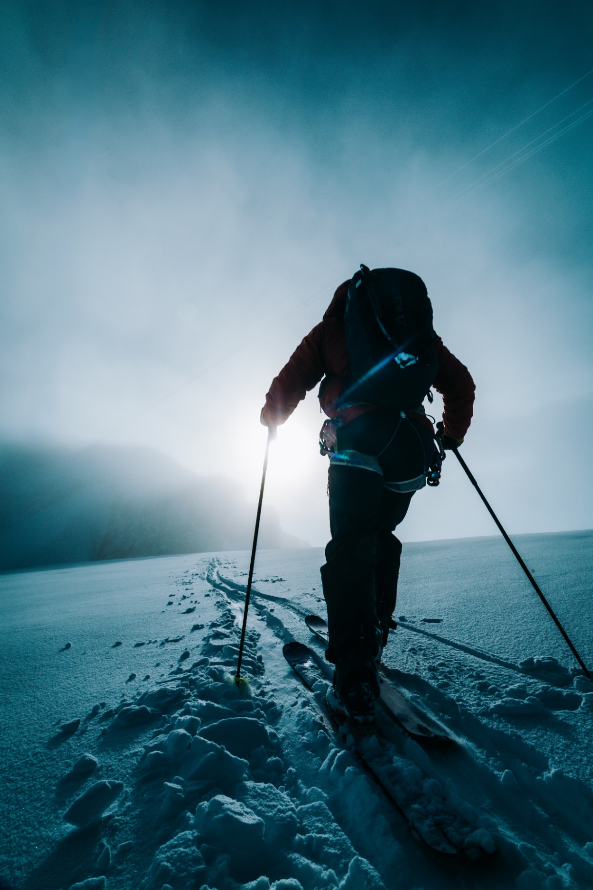 Ski tourer climbing backlit in a red jacket