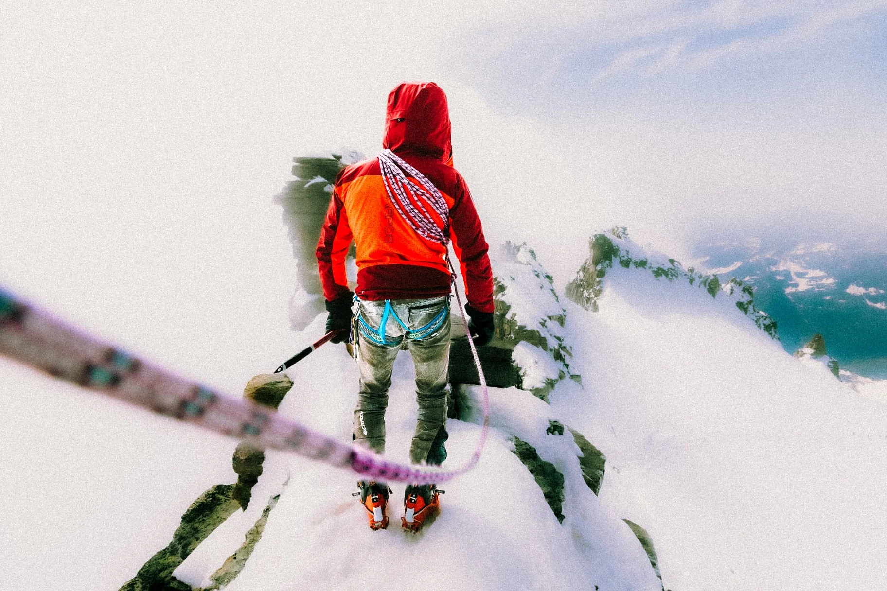 Alpinist in a red jacket holding the rope on a snowy ridge